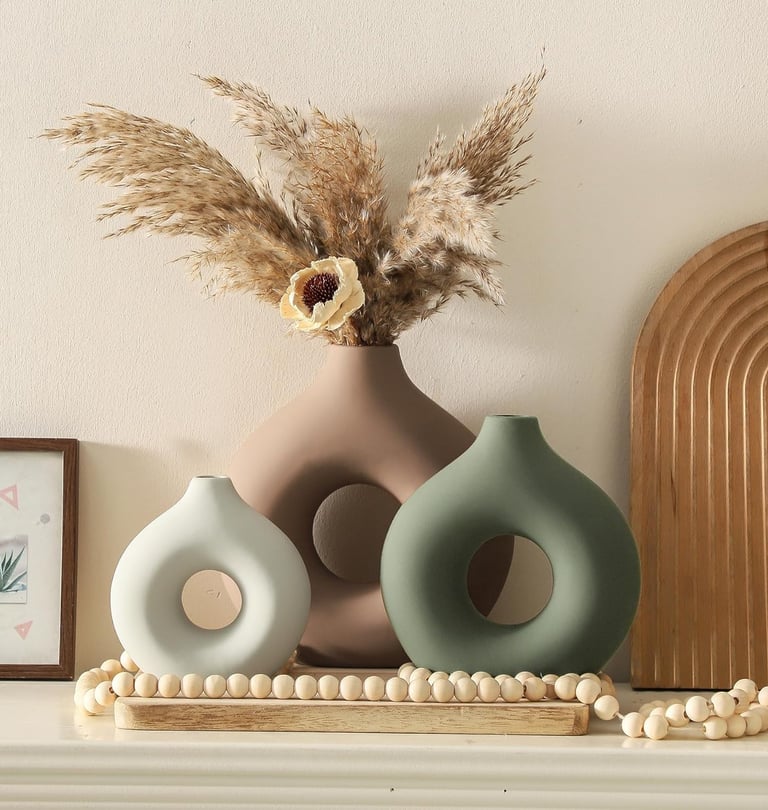 Modern donut-shaped ceramic vases in neutral tones with pampas grass on a mantle decor display.