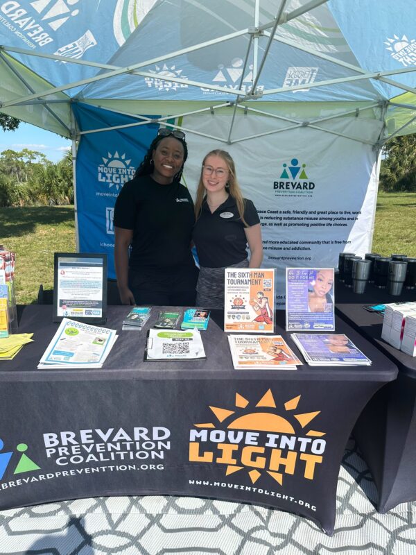 two women smiling in front of a table offering free information about move into light initiative