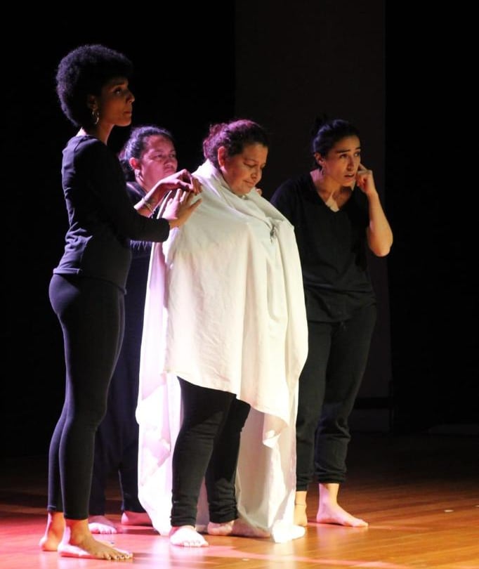 un grupo de actrices migrantes de pie en un escenario actuando