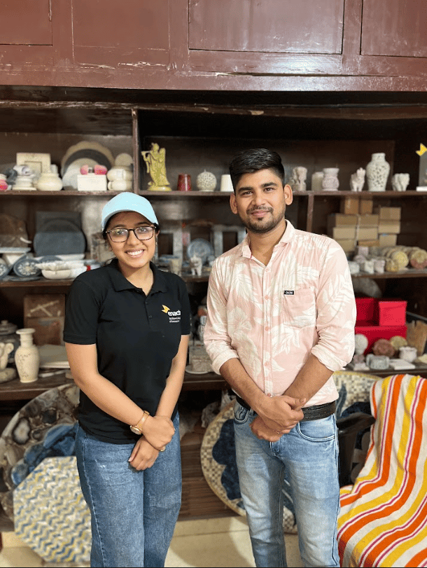 Team member and artisan standing in front of a shelf of  gaurahari products.