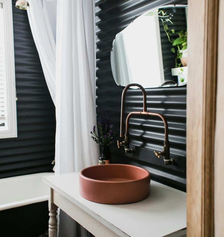 Modern bathroom with round basin and copper tap against dark panel wall