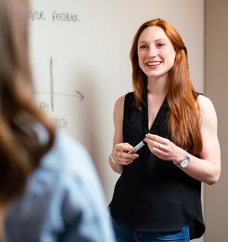 a woman in a black top and jeans standing in front of a white board