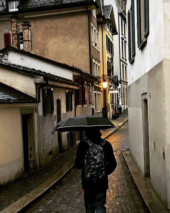A person walks through narrow alleys holding their umbrella in rainy Switzerland photography by LV