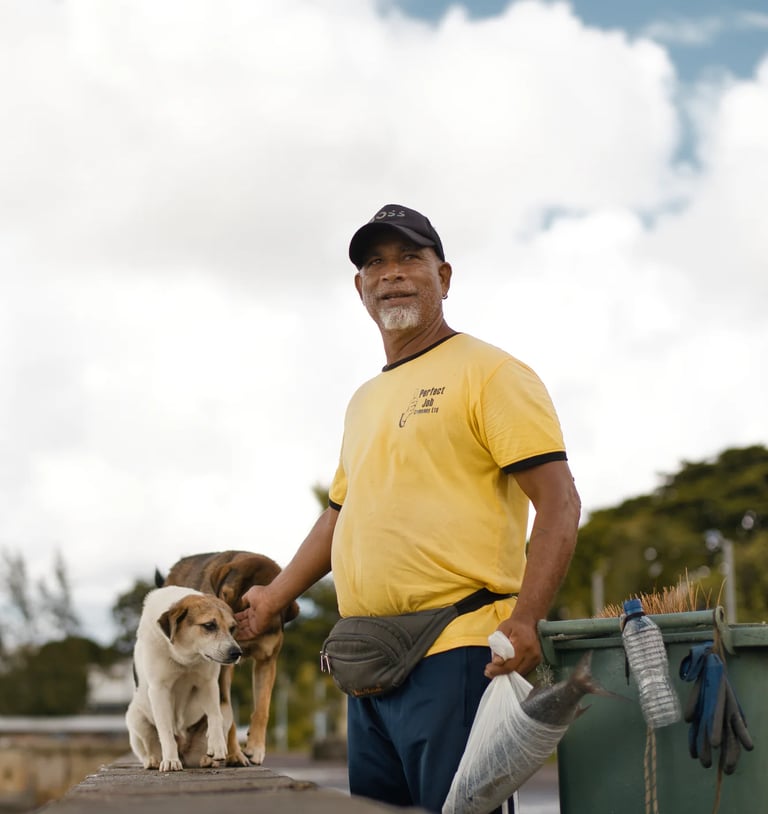 Waterfront cleaner with two stray dogs on Mahebourg jetty, Mauritius