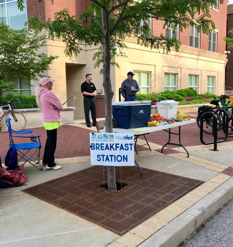 People standing around a table with food and drink behind a sign that reads "Breakfast Station"
