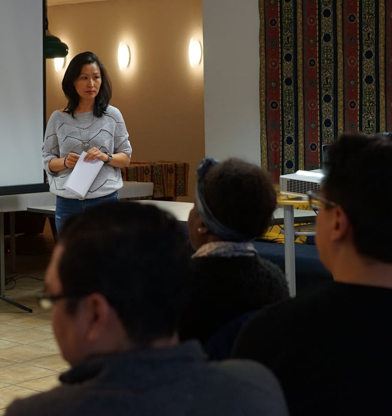 A professional woman presenting to a diverse audience during a business workshop or seminar.