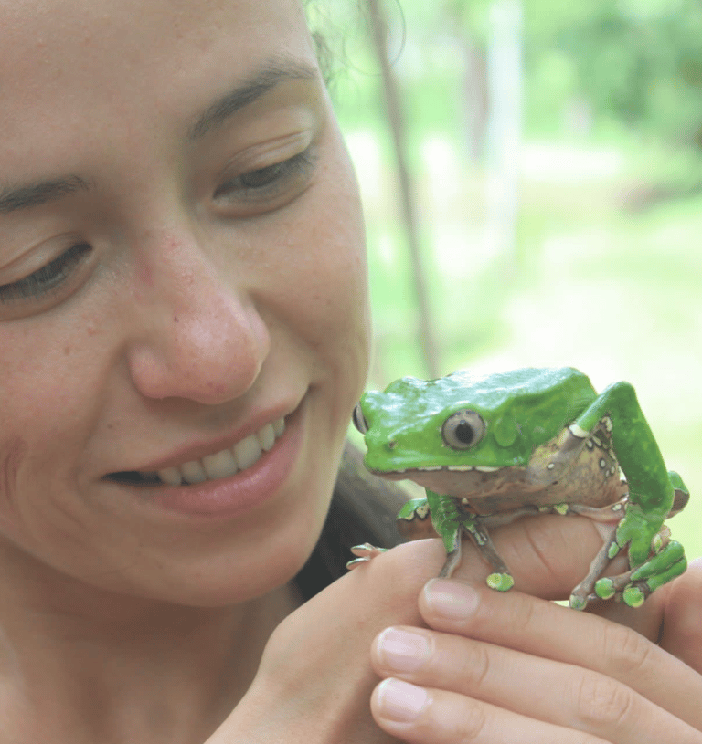 Smiling woman gently holding a large green frog, looking at it with affection. 