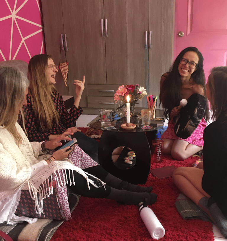 Group of women sitting in a cozy, colorful room around a low table with candles and flowers.