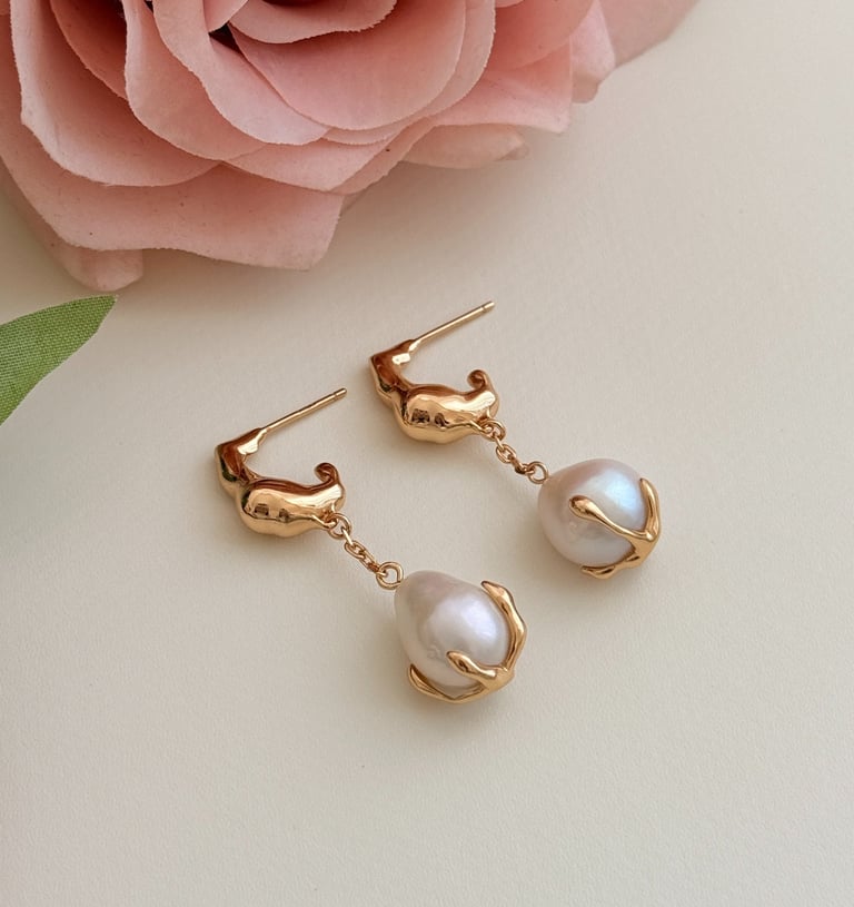 ein natürlicher Perlenohrring, der wie eine Rosenblüte aussieht, und eine Rose auf einem weißen Tisc