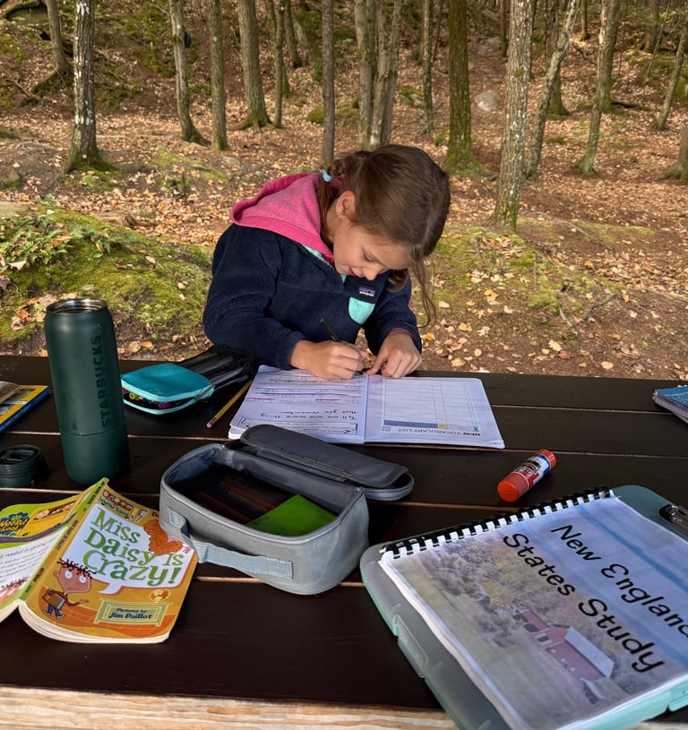 a young child is writing in a journal while road schooling at a picnic table at our campsite