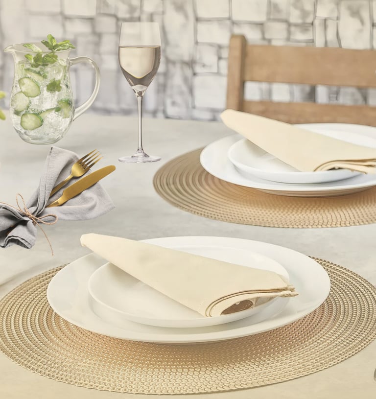 Mesa posta sofisticada em tons neutros com sousplat dourado, taças e guardanapos dobrados.