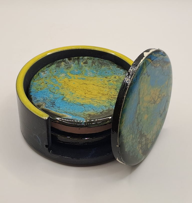 Handmade acrylic pour coasters with blue and yellow marble patterns in a black holder.