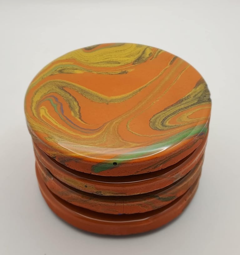Stacked orange marble resin coasters with swirled yellow and green patterns.