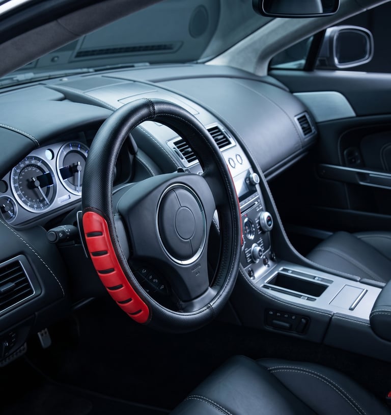 Luxury car interior featuring a black leather steering wheel with a red and black grip cover.