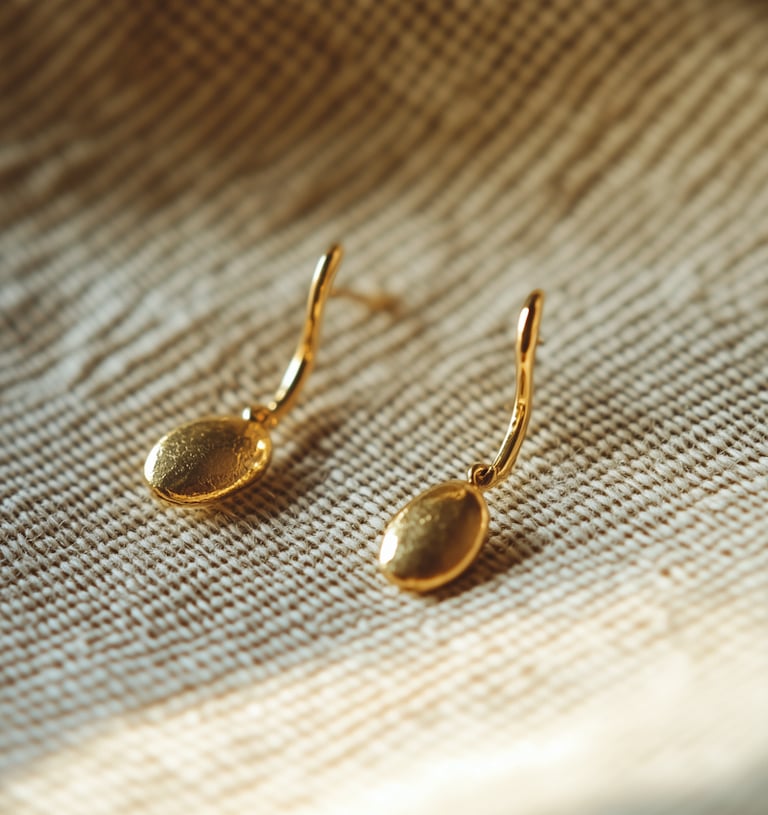 Elegant gold drop earrings with a textured oval design on a neutral linen fabric background.
