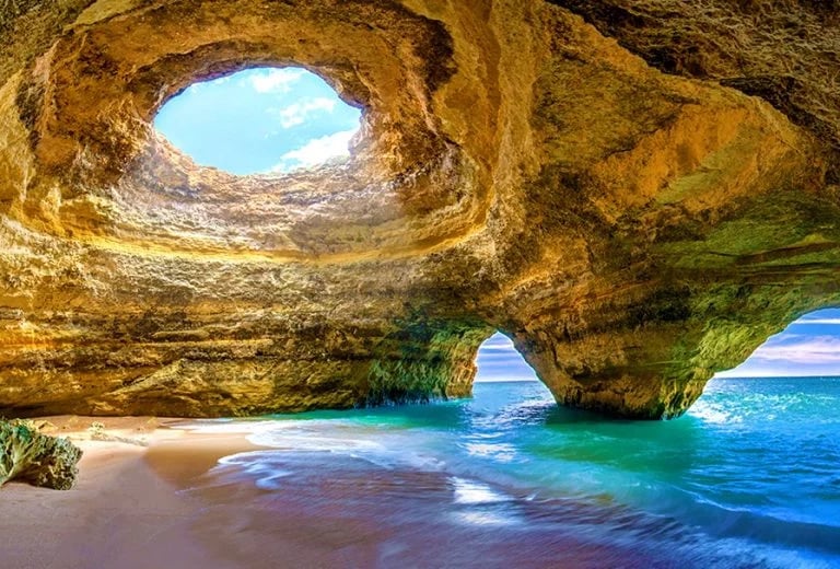 Scenic Benagil Cave in Algarve Portugal with sunlight streaming through the natural skylight onto the beach.