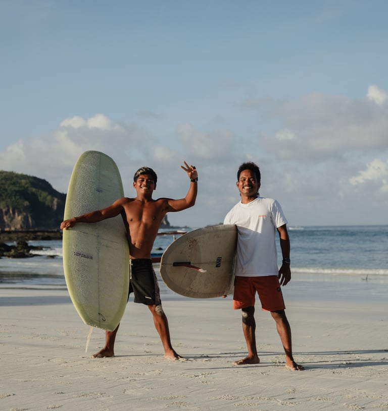 Two surf instructors at a surf school in Kuta Lombok holding boards on beach, offering surf lessons.