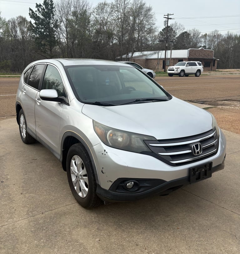 Silver Honda CR-V crossover SUV parked on a concrete lot with minor front bumper damage.