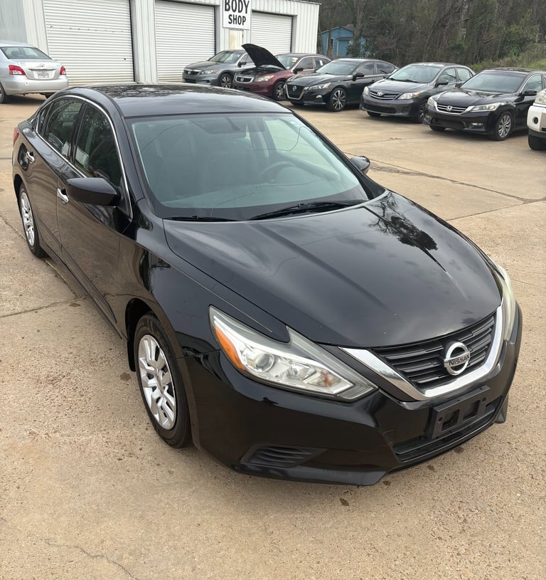 Black Nissan Altima sedan parked at an auto body shop and car repair lot.