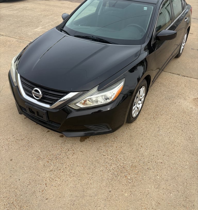 Black Nissan Altima sedan parked on a concrete lot at a used car dealership.