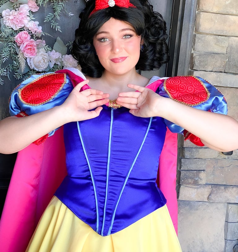 A woman in a Snow White princess cosplay dress with a red bow and floral background.