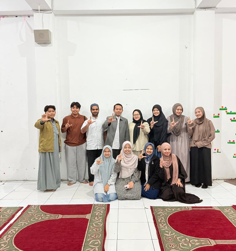 A group of Muslim students in a prayer room making hand gestures on red patterned rugs.
