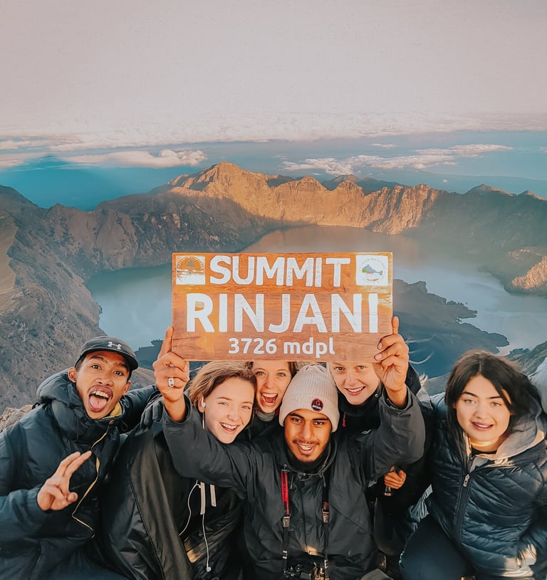 Hikers celebrating at Mount Rinjani summit with crater lake views in Lombok, Indonesia.