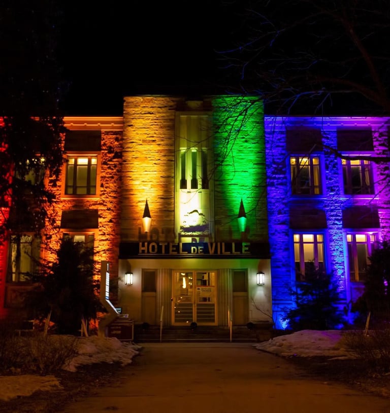 The Hotel de Ville building illuminated with bright rainbow pride colors at night.