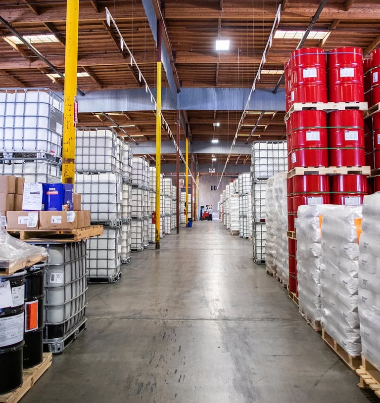 Warehouse with barrels stacked on pallets, filled with various chemicals