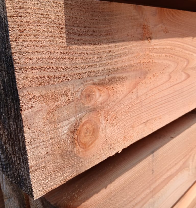 Stacked rough-cut cedar lumber showing natural wood grain and knots for construction projects.
