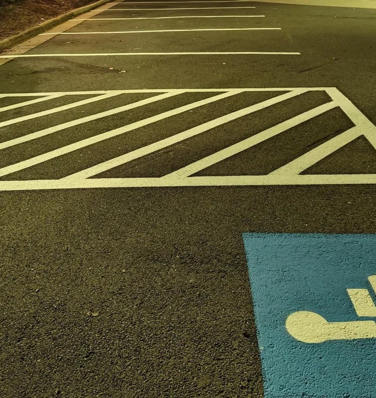 Hatched access aisle and ADA blue marking with clean striping near a sidewalk at night.