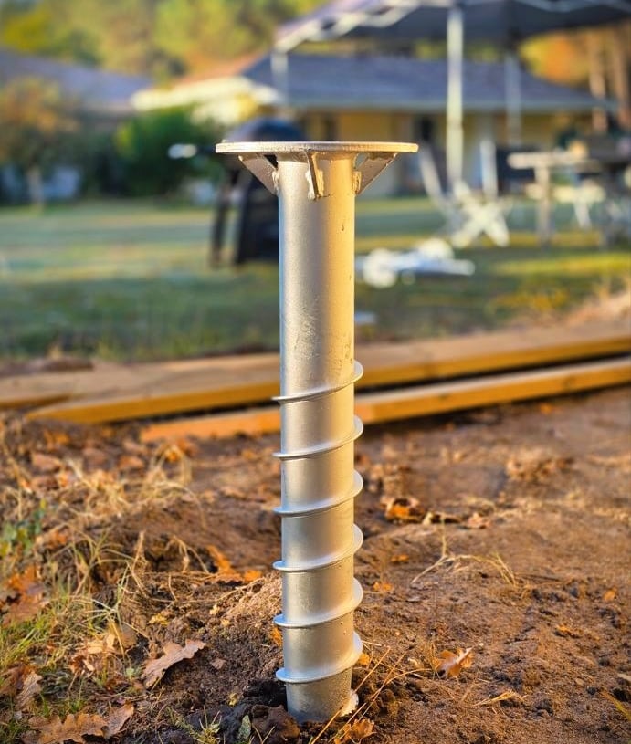Galvanized steel helical pile foundation screw installed in the ground for deck construction.