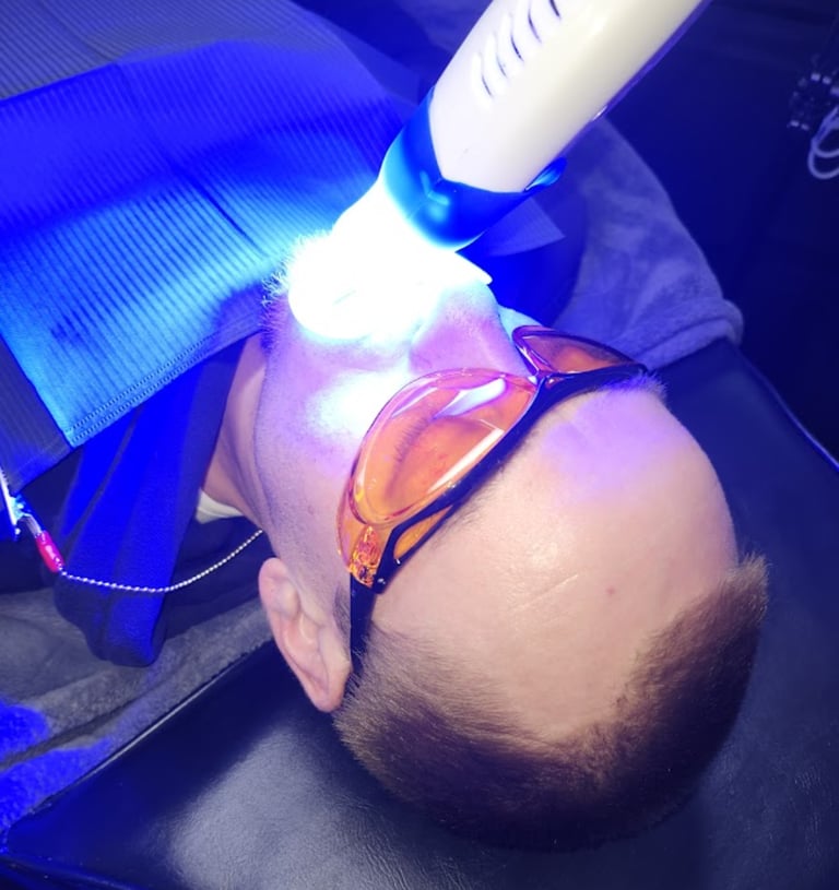 Patient receiving professional laser teeth whitening treatment with protective eyewear at a dental clinic.
