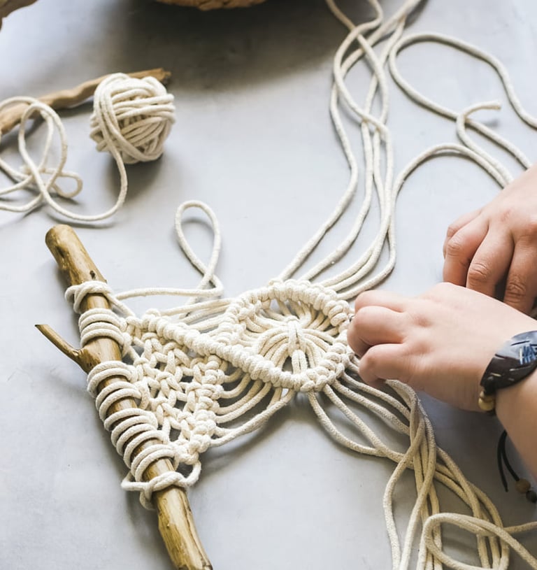 Manos creando un tapiz de macramé estilo boho utilizando cordón de algodón blanco.