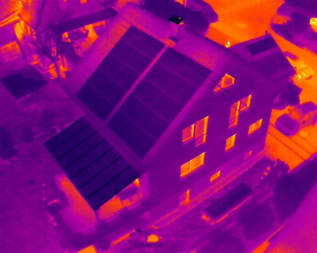 Aerial thermal imaging scan of a house showing heat loss through windows and energy-efficient solar panels.