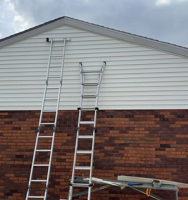 Two aluminum extension ladders leaning against a house with white siding and brick for home repair work.