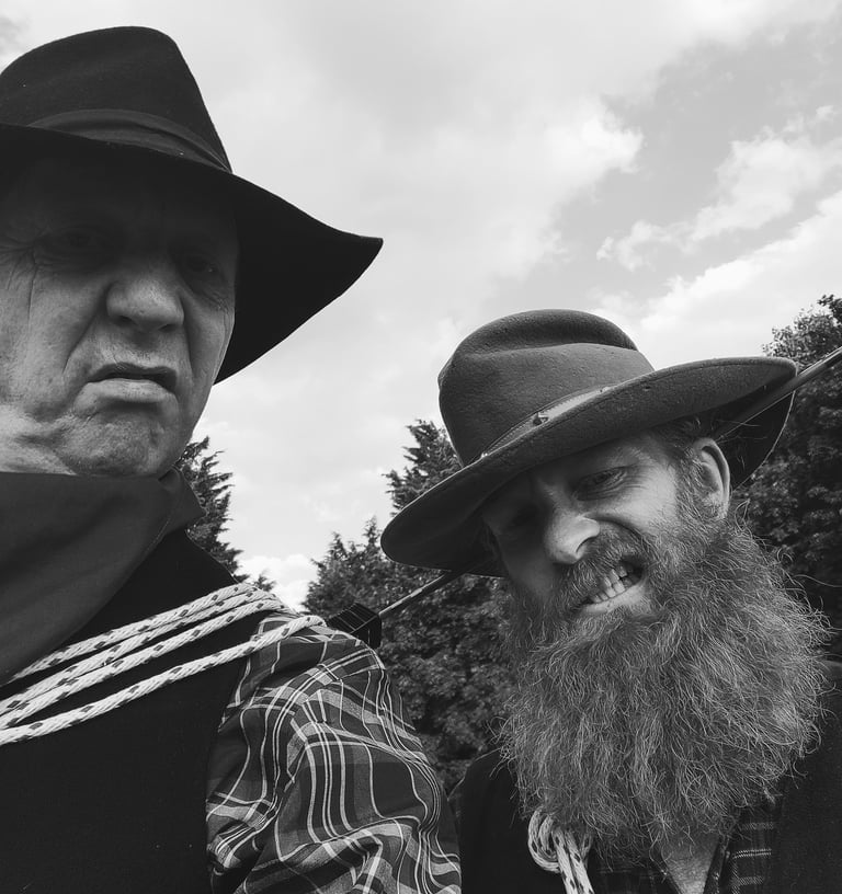 Black and white portrait of two rugged men in cowboy hats with long beards and western attire.