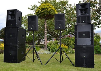 Professional outdoor sound system with black PA speakers and subwoofers on tripod stands.