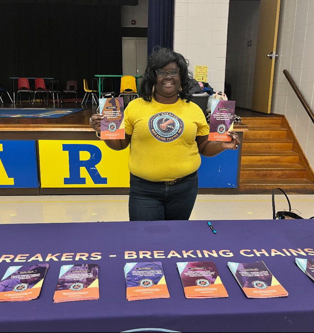 A smiling woman at a Cycle Breakers Breaking Chains Inc. event holding community outreach brochures.