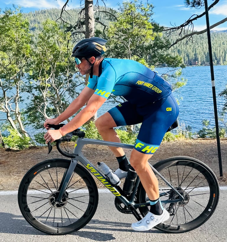 A man on a bike wearing a cycling kit in the outdoors by a lake