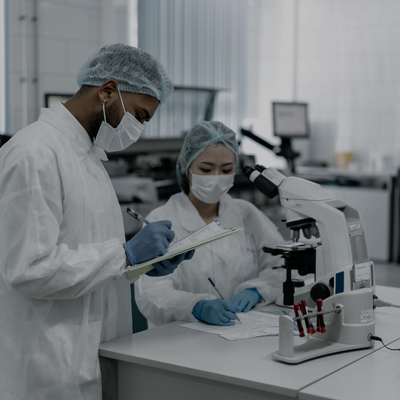 two people in lab coats and masks are looking at a microscope