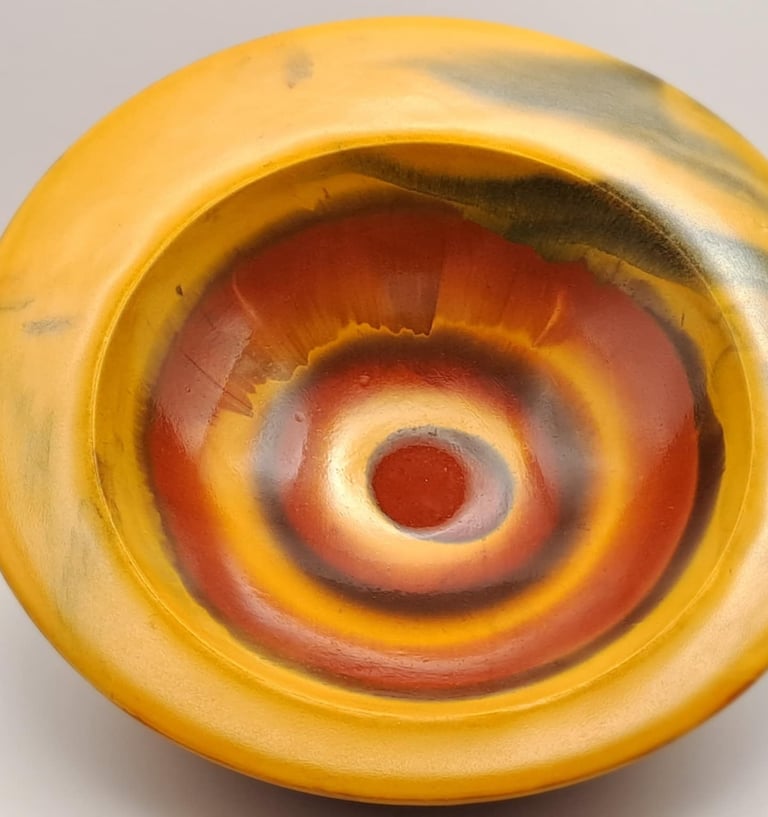 A decorative handcrafted bowl featuring a yellow rim and concentric orange rings with a glossy finish.