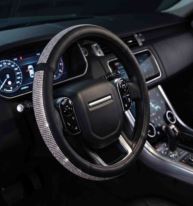Black leather car steering wheel cover with sparkling rhinestone accents in a luxury vehicle interior.