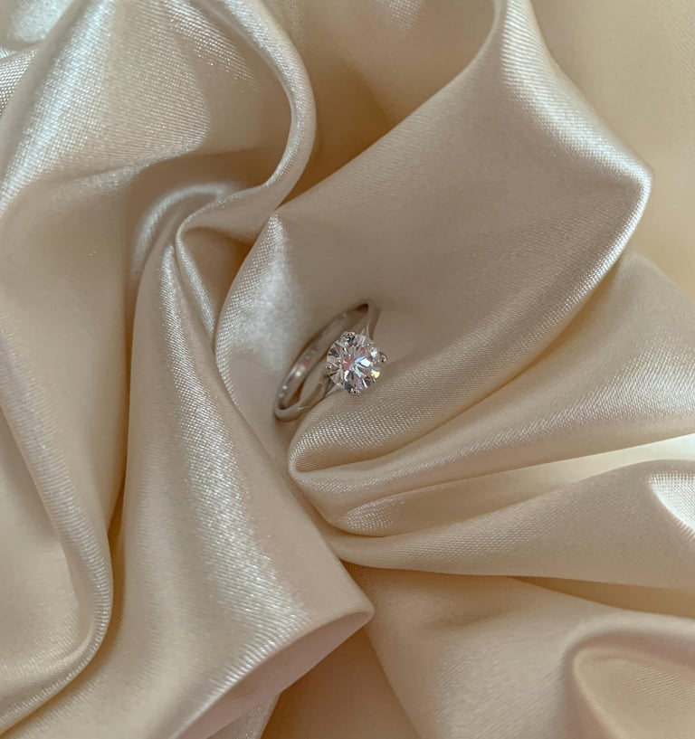 Elegant round-cut diamond engagement ring nestled in folds of ivory silk fabric.