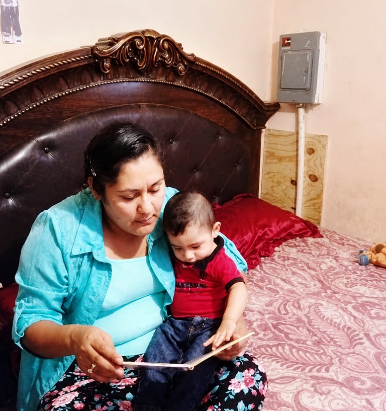 Mother reading a book with her toddler son while sitting on a bed.