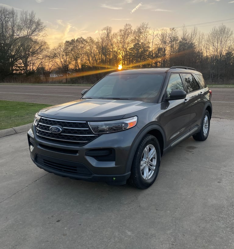 A gray Ford Explorer SUV parked on a concrete lot during a golden hour sunset.