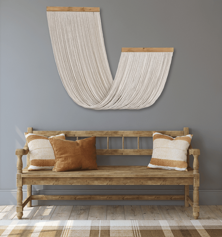 A Wall Hanging Made with Cotton Rope Suspended from Wooden Board that is Hung Above a Wooden Bench