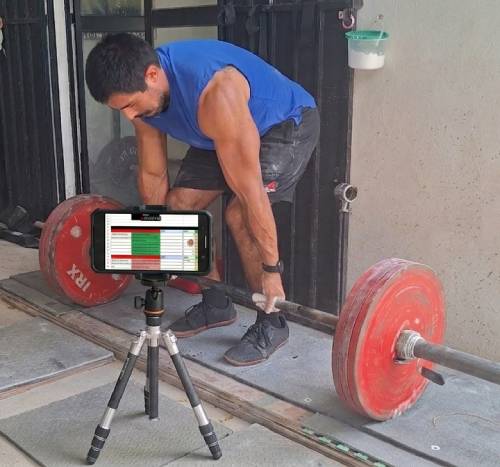 Una persona haciendo peso muerto mientras tiene su entrenamiento en el teléfono