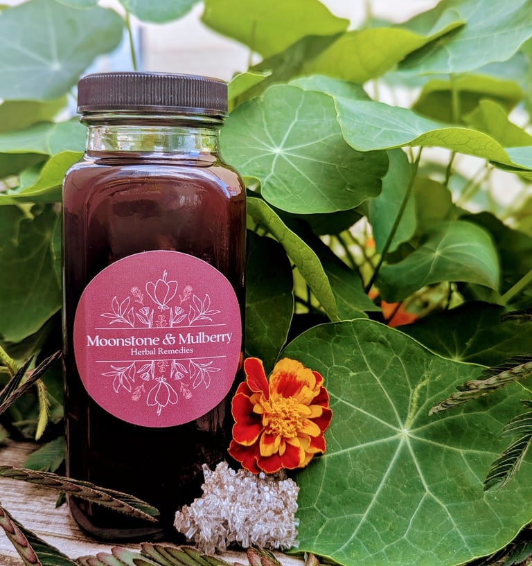 Bottle of elderberry oxymel with nasturtium leaves in the background and a marigold and crystal next to it.