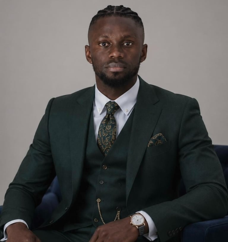 A professional man in a tailored dark green three-piece suit with a patterned tie and gold pocket watch chain.